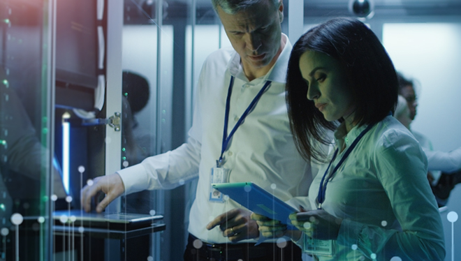 Image shows a two people woking together in a Data Server Machine room collecting information. 