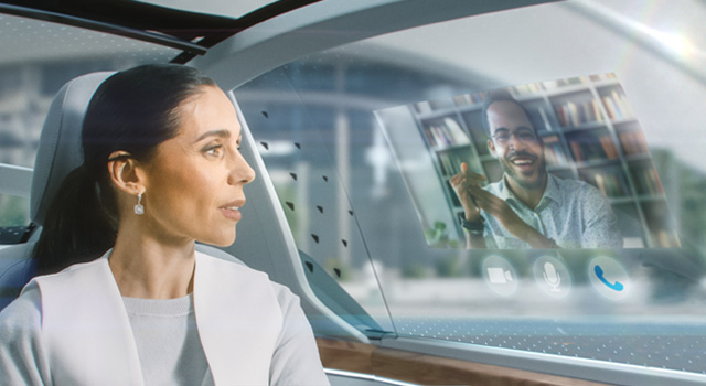 Woman sitting in autonomous vehicle chatting on a VR video conference screen overlaid on the car window.