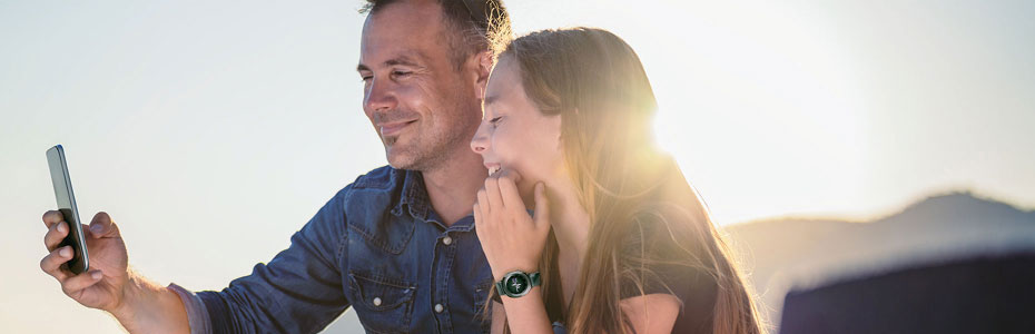 Man and teenage girl smile taking selfie outdoors at sunset, both joyful and content.