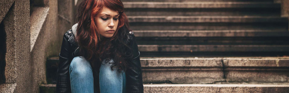 Young woman with reddish-brown hair sits on concrete steps, looking thoughtful.