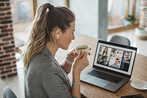 A woman in a video conference wearing wireless earbuds, while drinking coffee