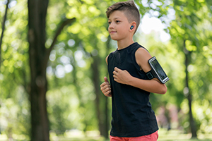 A teenage boy jogging in the park with wireless earbuds
