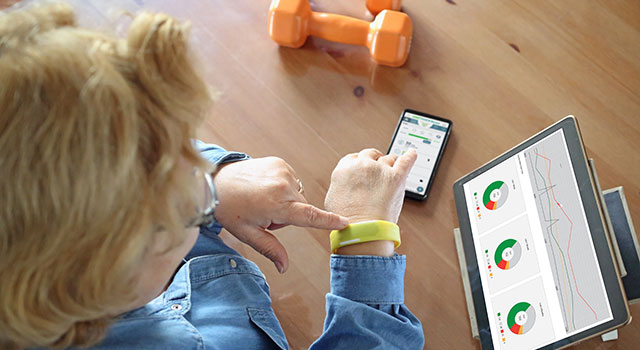 Senior woman with fitness tracker uses smartphone, tablet nearby.