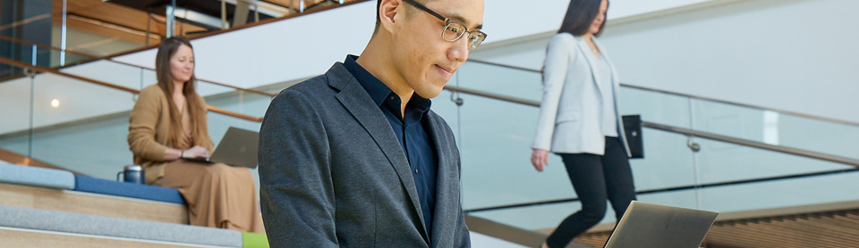 Man working on laptop while sitting on steps within a modern building