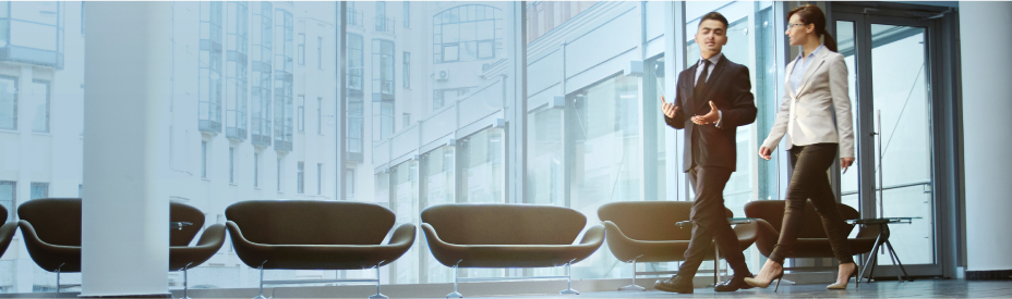 Man and woman business professionals in an office walkway with windows and love seats