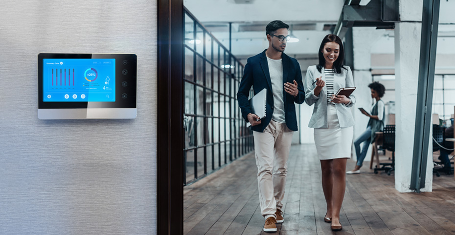 Two people walking down office hallway with smart building technology shown.