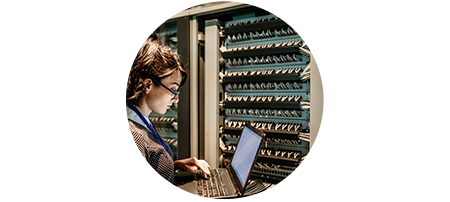 Woman looking at a laptop computer in a technology environment and server machines behind her.