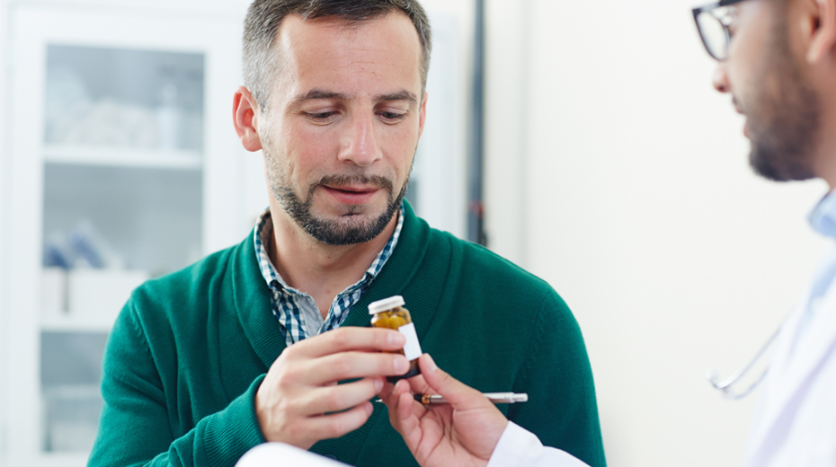 Image shows a male patient in a Doctor's office setting. His Doctor is handing him a medical prescription during this visit.