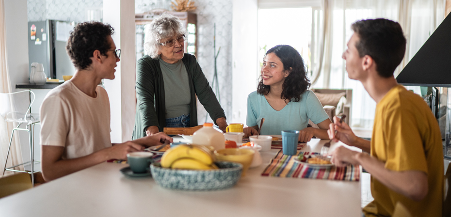 Image shows a family of younger generation having a meal while talking with their grandmother.