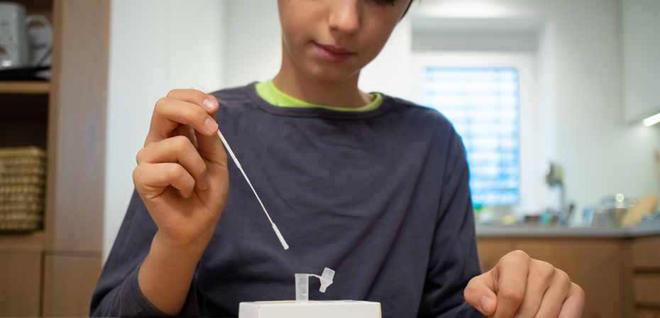 Image shows a person taking sample and applying to an 'At-Home' rapid test kit as a Point-of-Care Test.